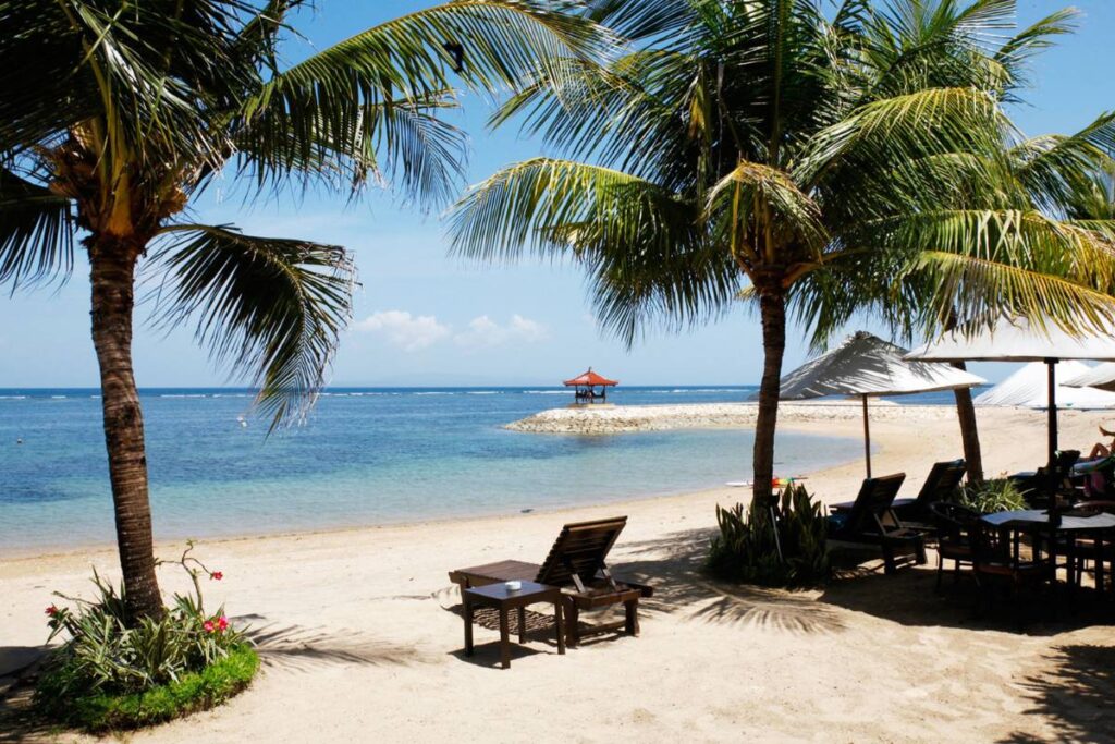 Beach view with palm trees, lounge chairs, and gazebo in Sanur, Bali