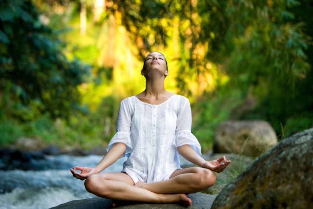 Woman in white practicing meditation by a river in a lush Bali forest