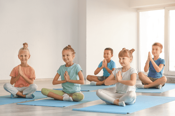 Children sitting cross-legged on yoga mats with hands in prayer pose