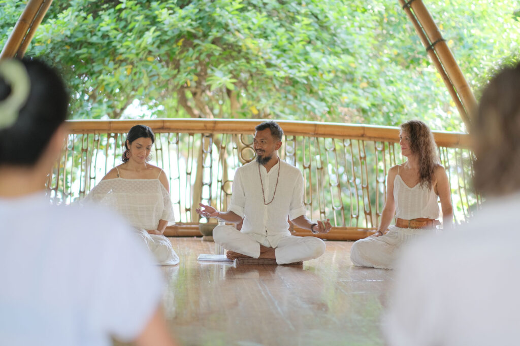 Yoga teachers Krishna, Sheryl, and Lisa sitting in white clothes during the YTT closing ceremony