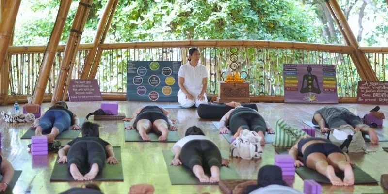 Ibu Dayu leading a Yin Yoga class in the bamboo shala at Power of Now Oasis in Sanur, Bali, with students lying in Sphinx Pose