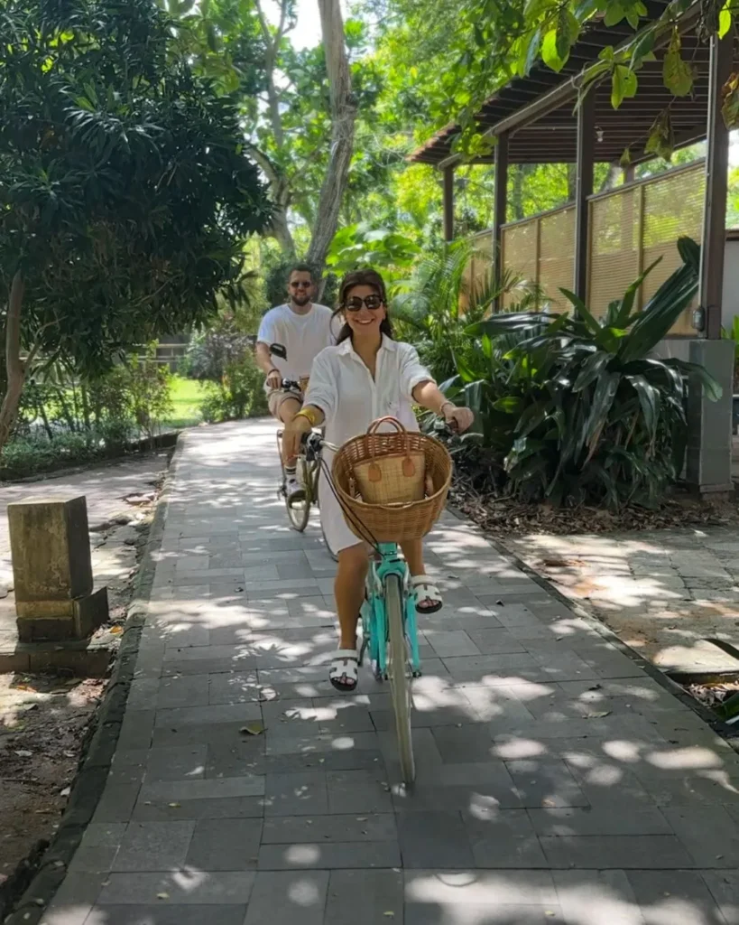 Couple riding bicycles through a shaded garden path in Sanur, Bali during a yoga retreat
