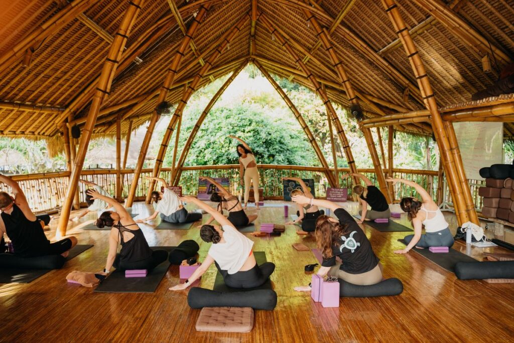 Yoga students practicing side stretches during class in an open-air bamboo shala in Bali
