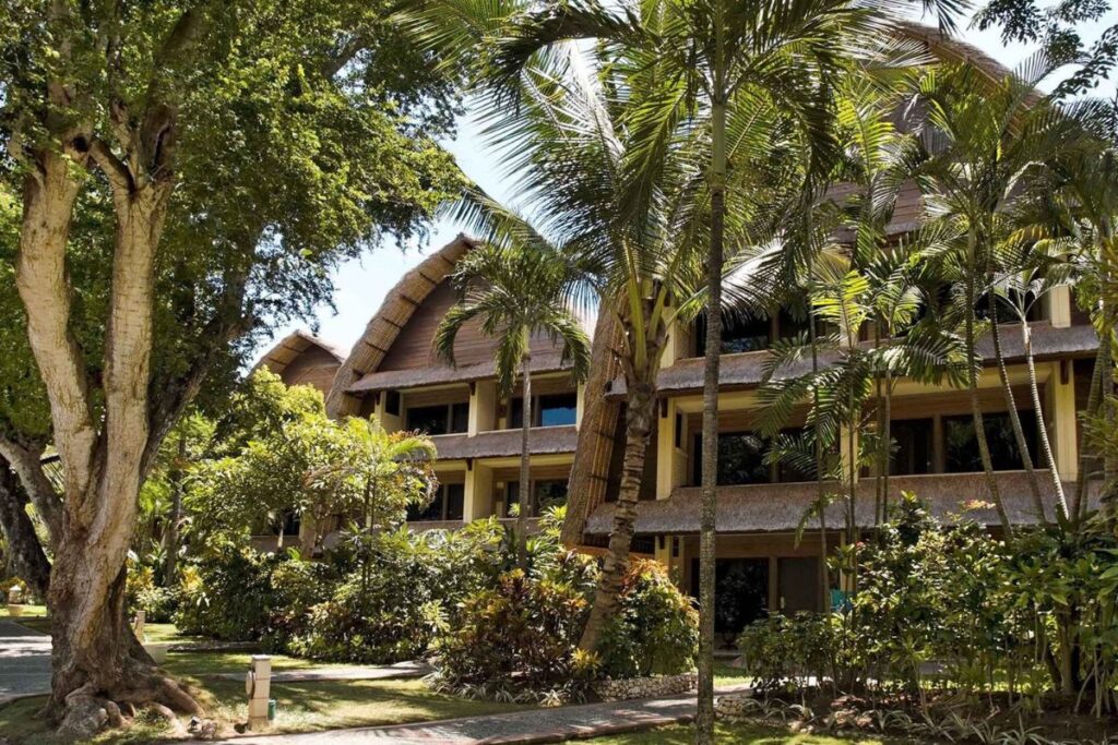 Thatched-roof buildings and tropical trees surrounding the rooms at Mercure Sanur Resort